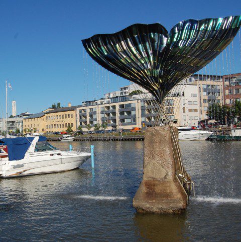 A boat is in the water near a statue of a whale tail.