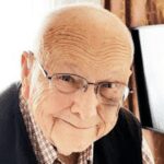 Elderly man smiling with glasses indoors.
