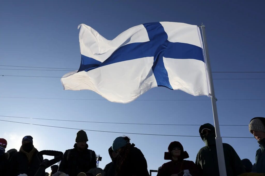 A group of people standing under a large finnish flag.
