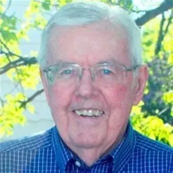 Elderly man smiling outdoors with greenery background.
